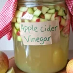 Jar of homemade apple cider vinegar with apple scraps on a marble counter