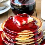Homemade blueberry syrup recipe poured over pancakes with fresh berries